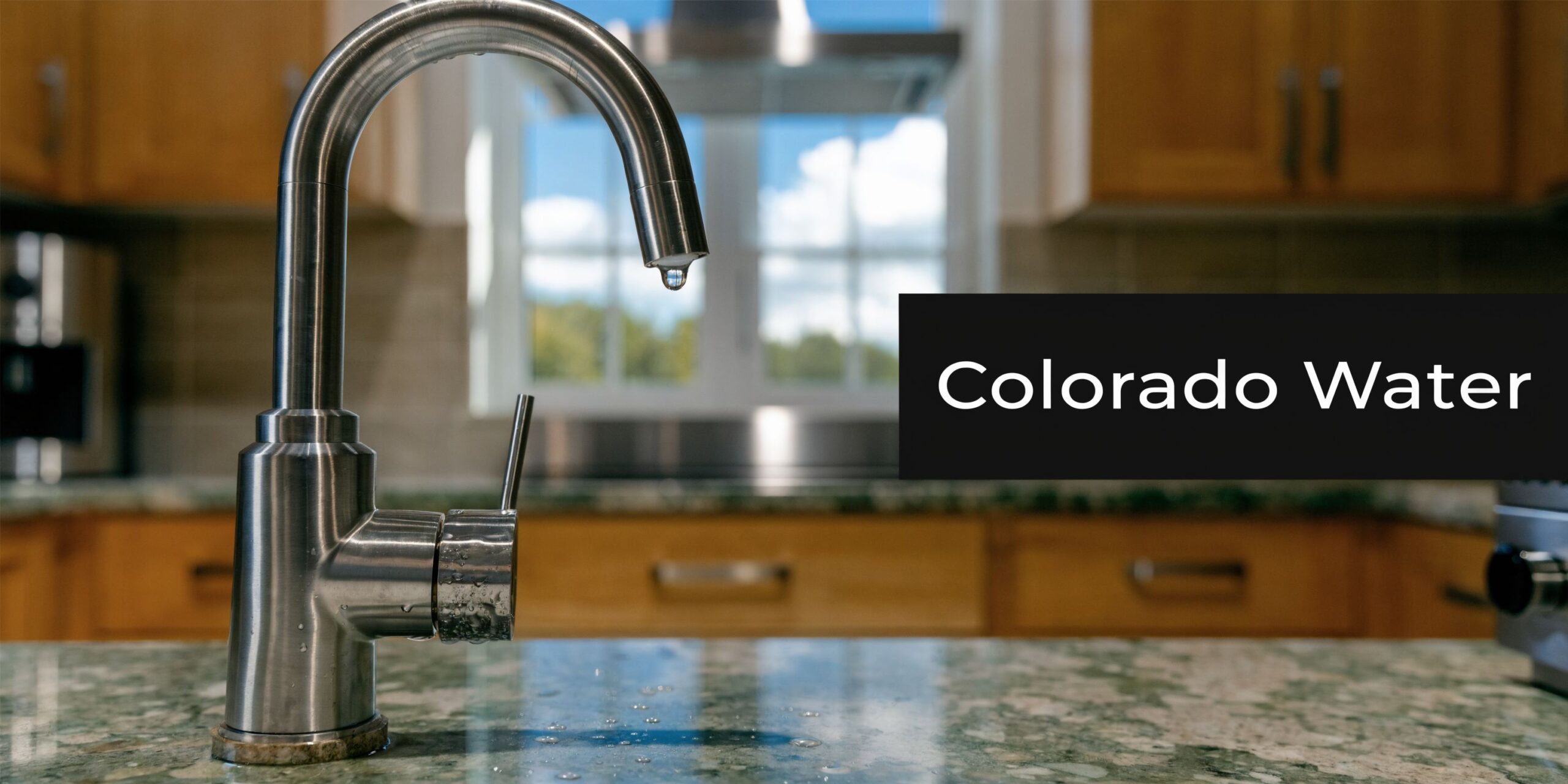 A stainless steel kitchen faucet with a single drop of water hanging from the spout on granite.