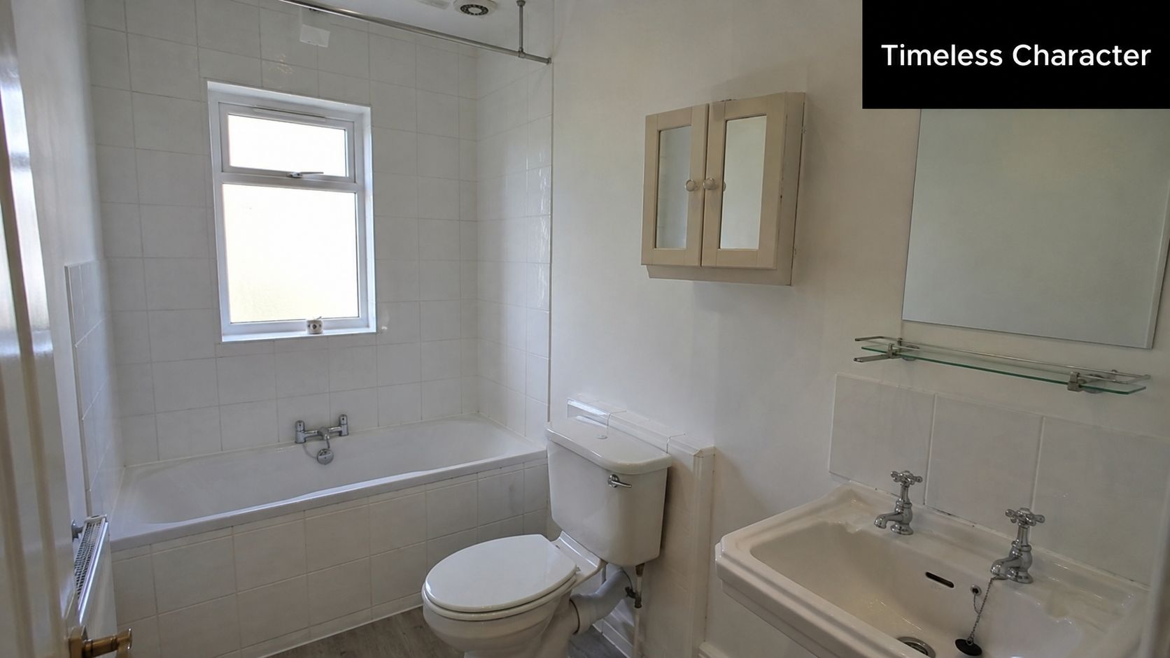 A clean, traditional bathroom interior featuring a white bathtub, toilet, and sink under a small window.