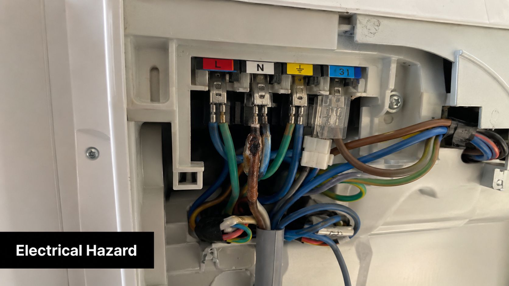 A close-up view of a damaged, scorched electrical terminal block inside an appliance causing a safety hazard.